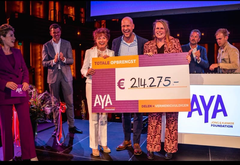 Dennis met anderen op het podium van het benefiet, met de cheque