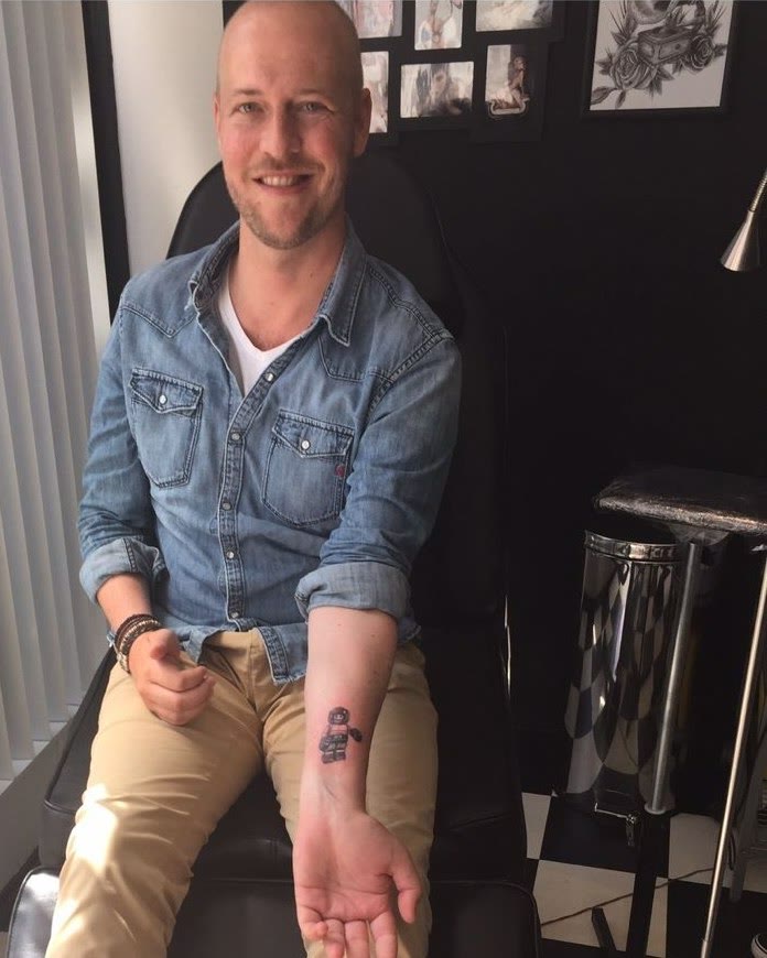 Dennis in de stoel van de tattooshop, het legopoppetje vers op zijn onderarm