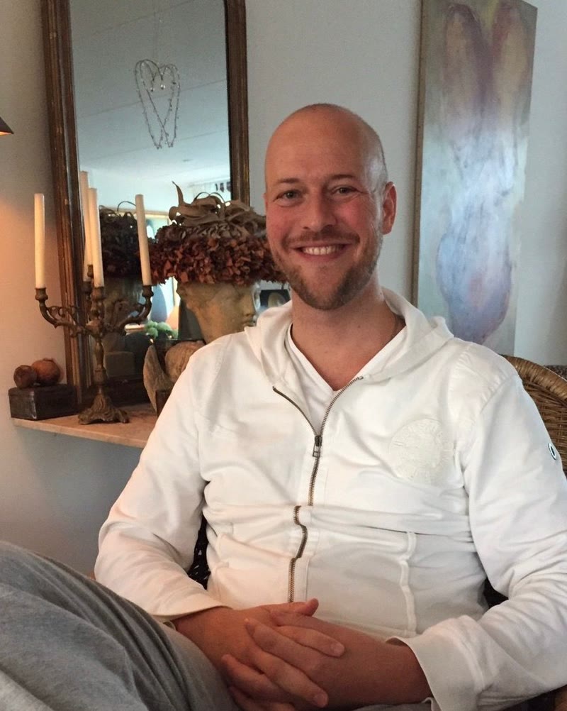 Dennis thuis in een rieten stoel, in een wit vest