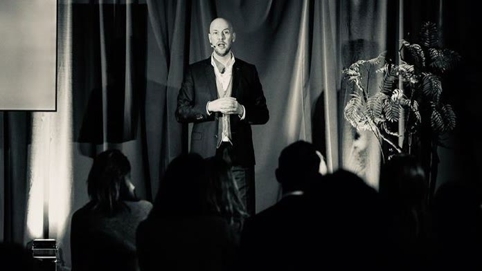 Dennis de Graaf op een podium voor een zaal in het donker